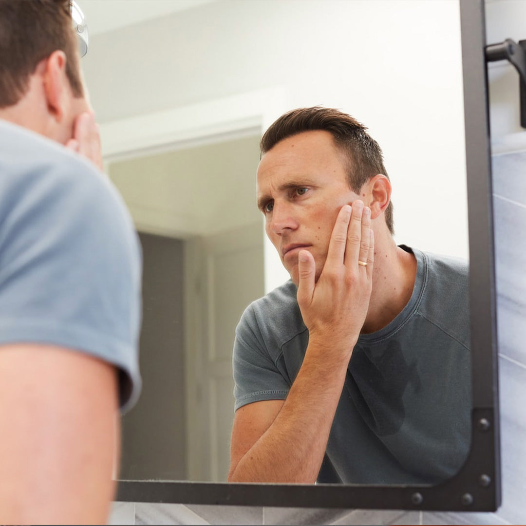 Man touching freshly shaved skin, looking in mirror