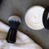 shaving brush laying next to oneblade shaving cream